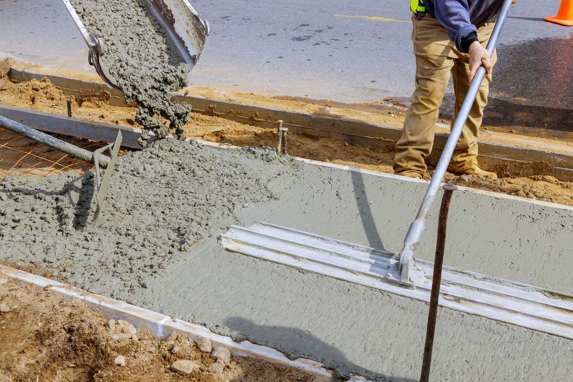 Construction worker pouring concrete into a curb form using a chute and screed.