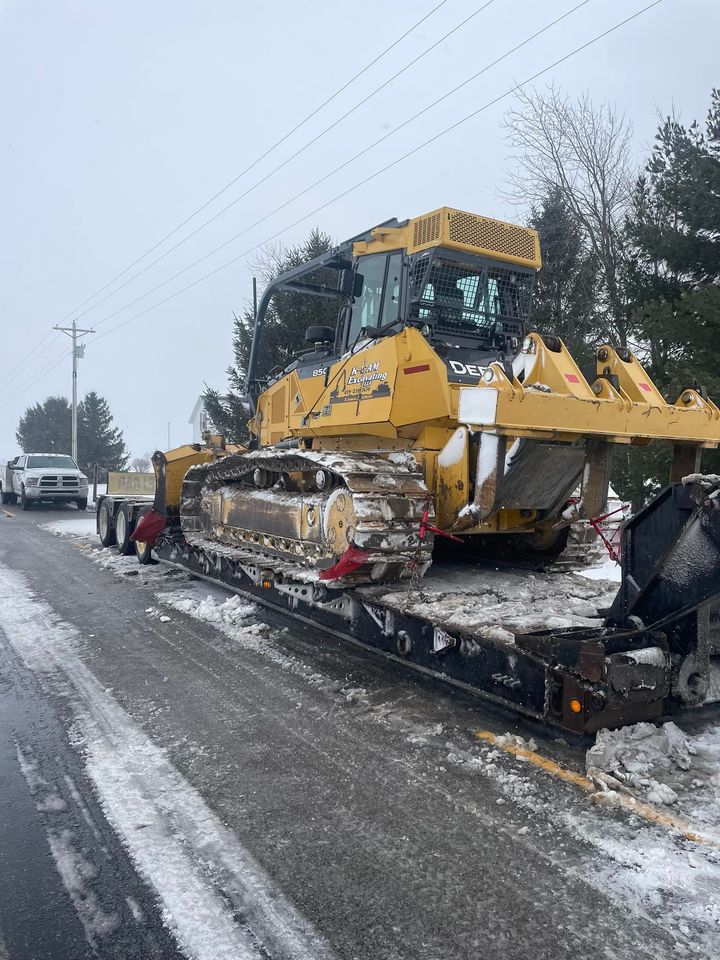 A bulldozer is sitting on top of a train on the side of the road.