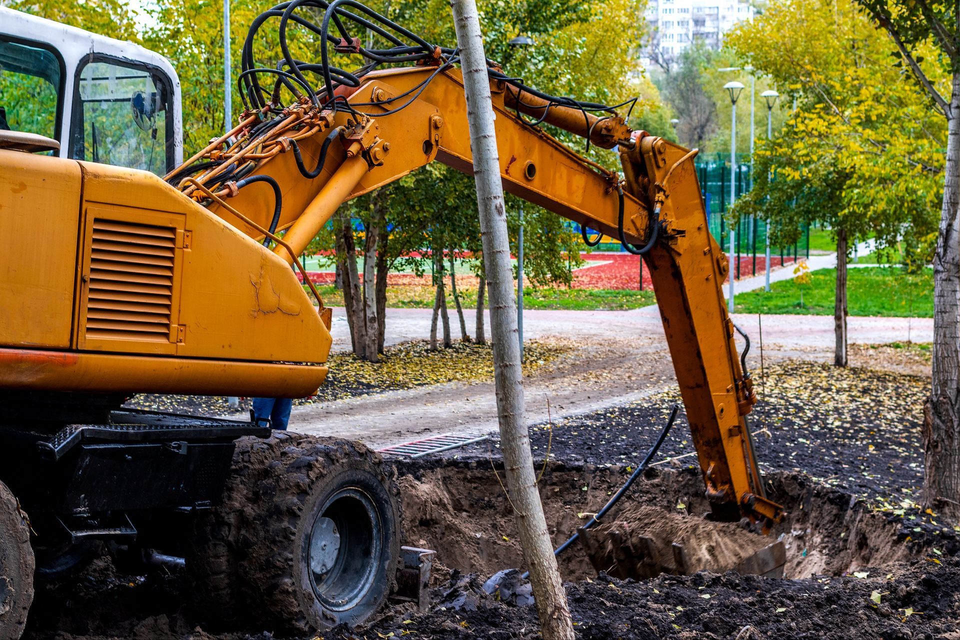 A yellow excavator with a large shovel scoop is digging up brown soil at a construction site