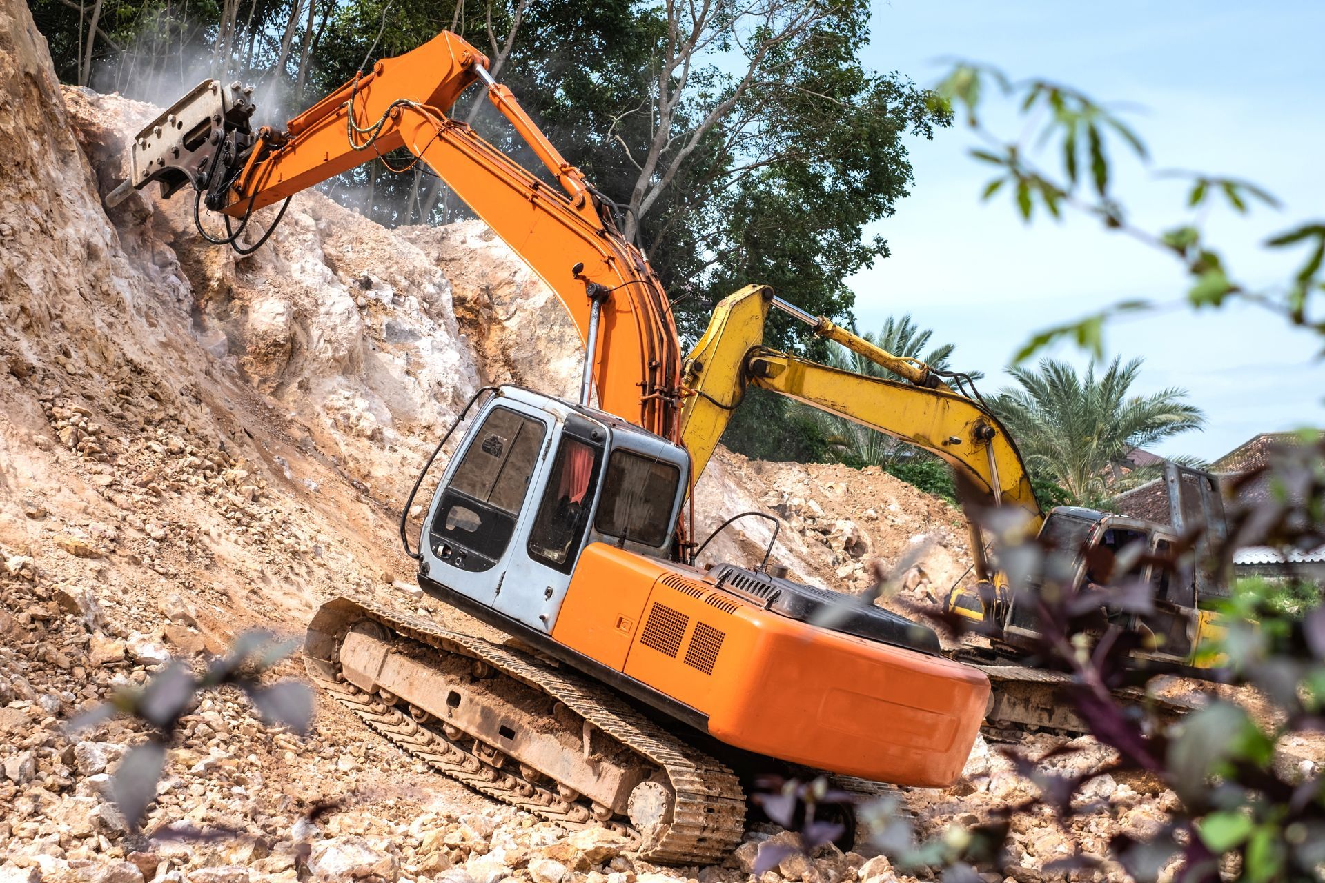 A large hydraulic jackhammer is actively at work, breaking apart rocks on a slope with forceful blows.