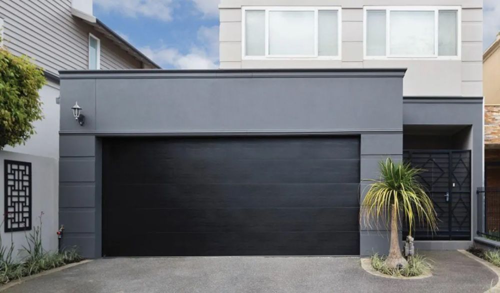 A Large House With a Black Garage Door and a Palm Tree in Front of It — Hastings Garage Door Services in Port Macquarie