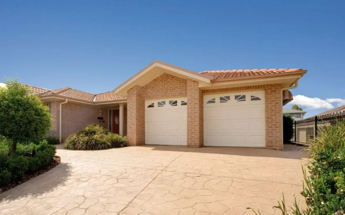 A Large Brick House With Two White Garage Doors and a Driveway — Hastings Garage Door Services in Port Macquarie