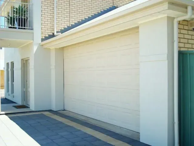 A white garage door is next to a brick building— Hastings Garage Door Services in Port Macquarie