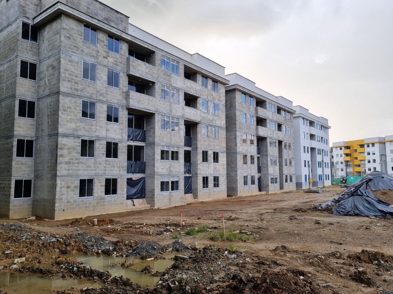 Una hilera de edificios de apartamentos de hormigón sin terminar, erigidos sobre un terreno fangoso bajo un cielo nublado.