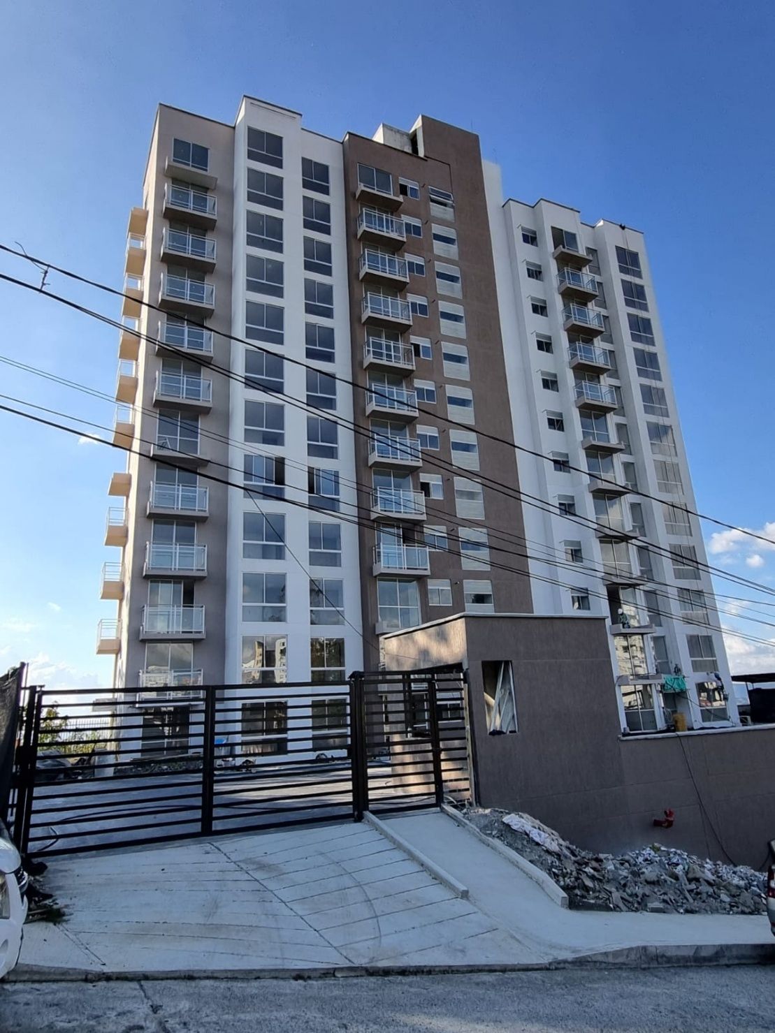 Un moderno edificio de apartamentos residenciales de varias plantas con balcones y entrada privada bajo un cielo azul despejado.