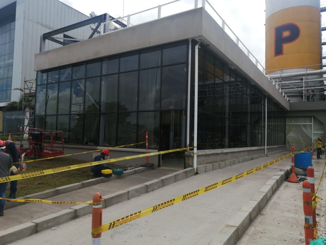 Obreros de la construcción cerca de un edificio moderno con paredes de cristal y un silo industrial amarillo con la letra