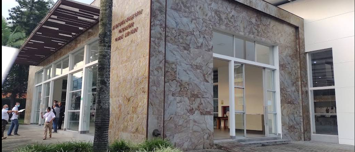 Edificio moderno con paredes de textura de piedra y grandes puertas de cristal, con un voladizo de madera, con gente de pie en las inmediaciones.