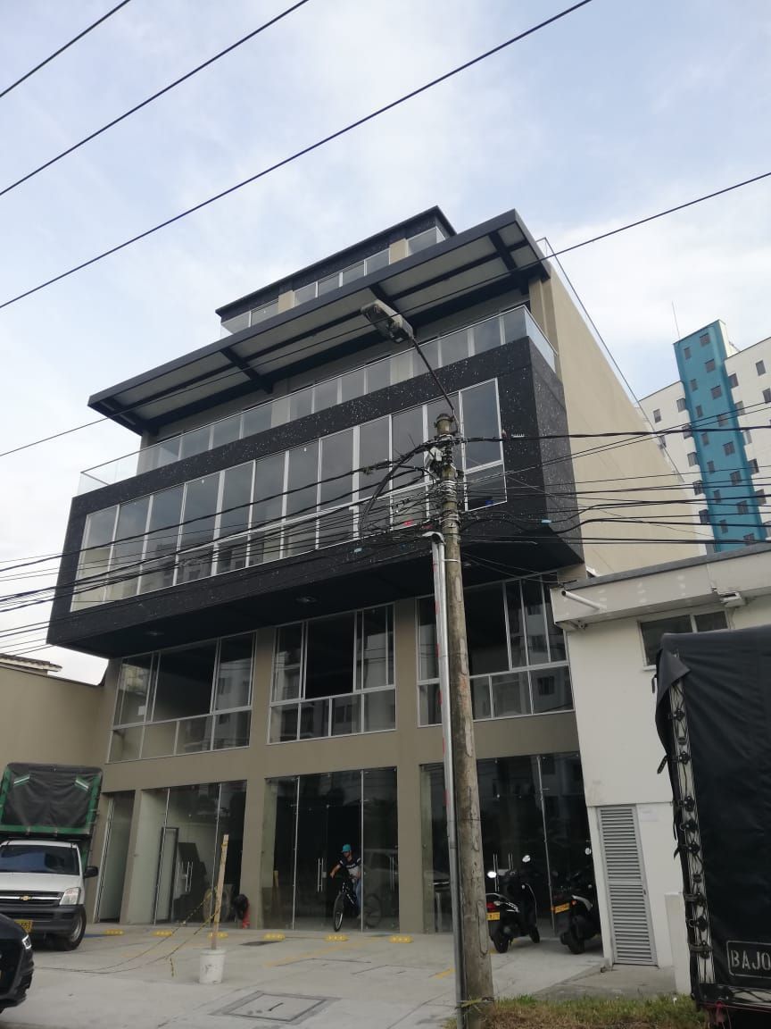 Un moderno edificio de varias plantas con fachada superior negra, grandes ventanales y un local comercial acristalado en la planta baja.