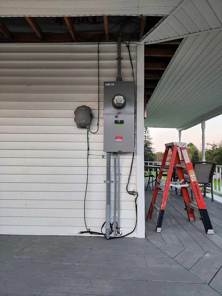 Red ladder beside a gray electrical meter panel on a house exterior porch
