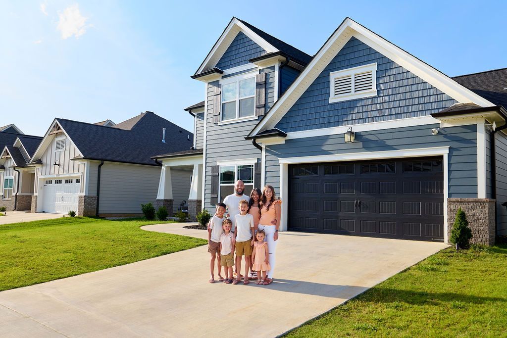 Family stands in front of a new house with blue siding and a dark garage door.
