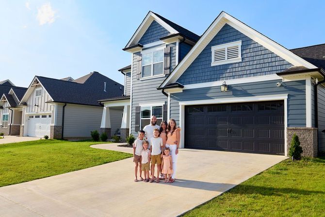 Family stands in front of a new house with blue siding and a dark garage door.