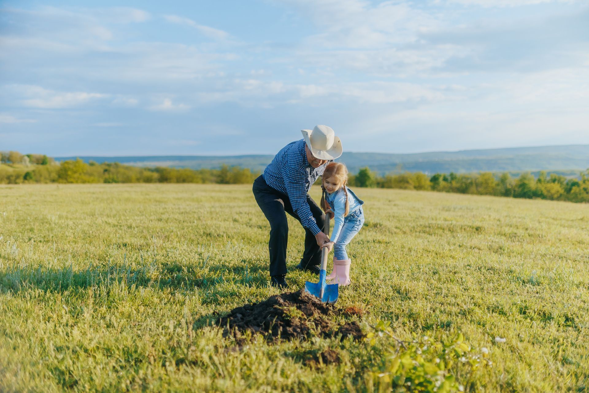 Man and child planting a tree in a sunny field.