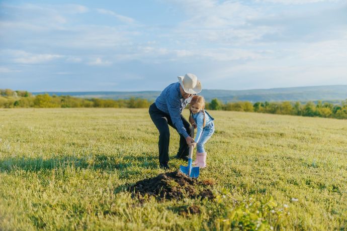 Man and child planting a tree in a sunny field.