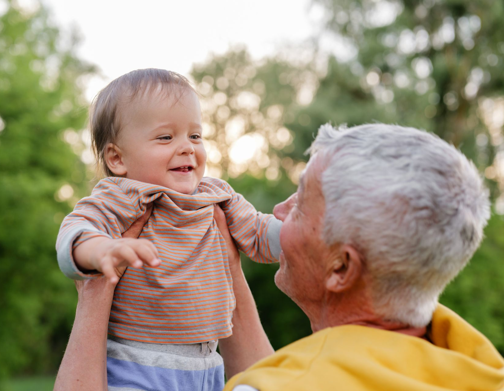 Smiling baby held up by older person outdoors.
