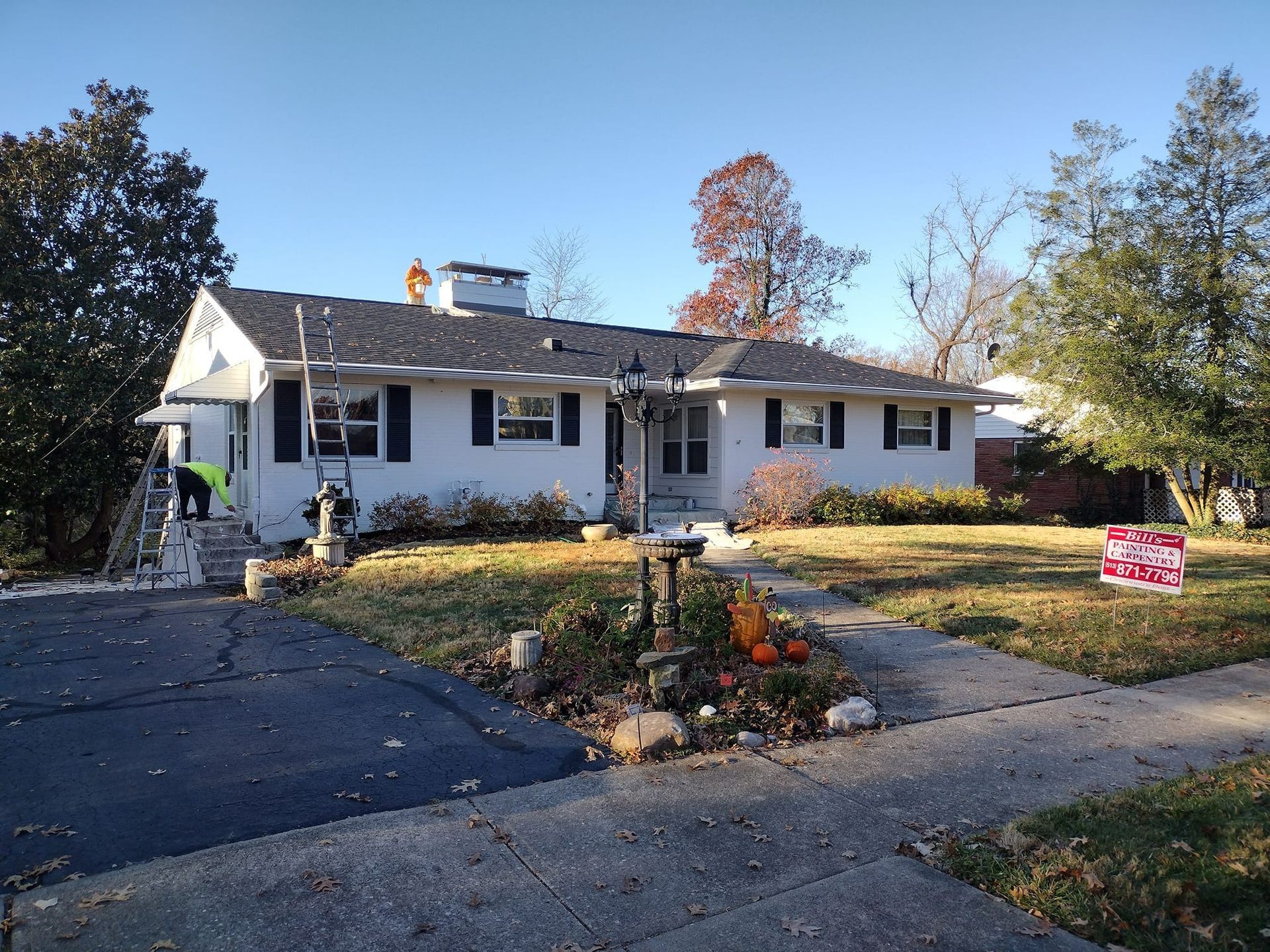 White house with black shutters and a new roof. A person works on a roof in the sun.