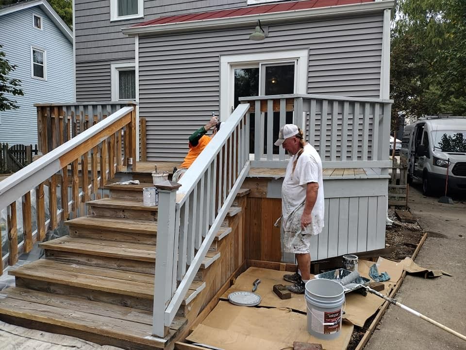 Man painting a deck and steps gray, with a partially visible building in the background.