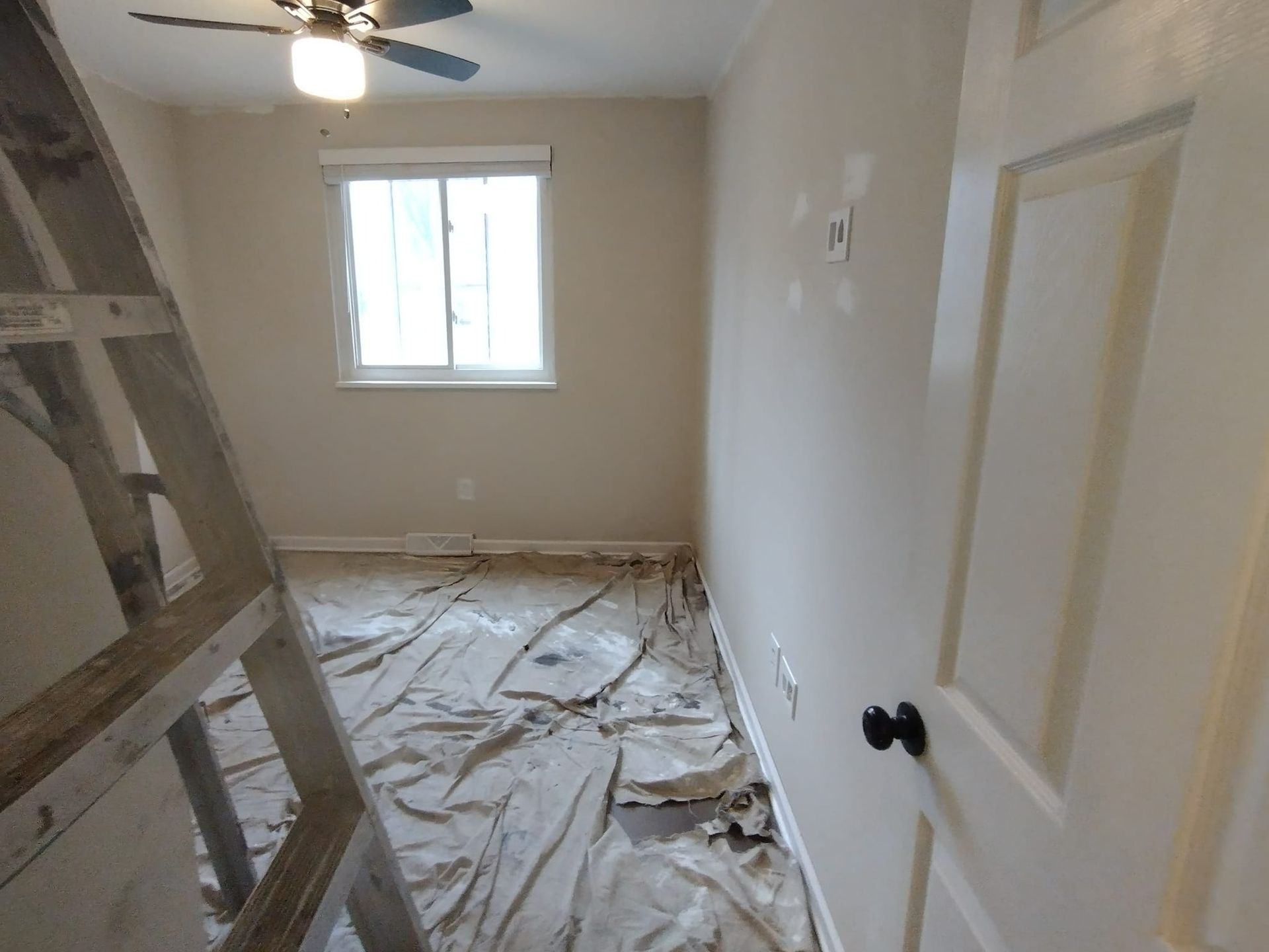 Room with ladder, drop cloths, and a window, appearing to be under renovation.