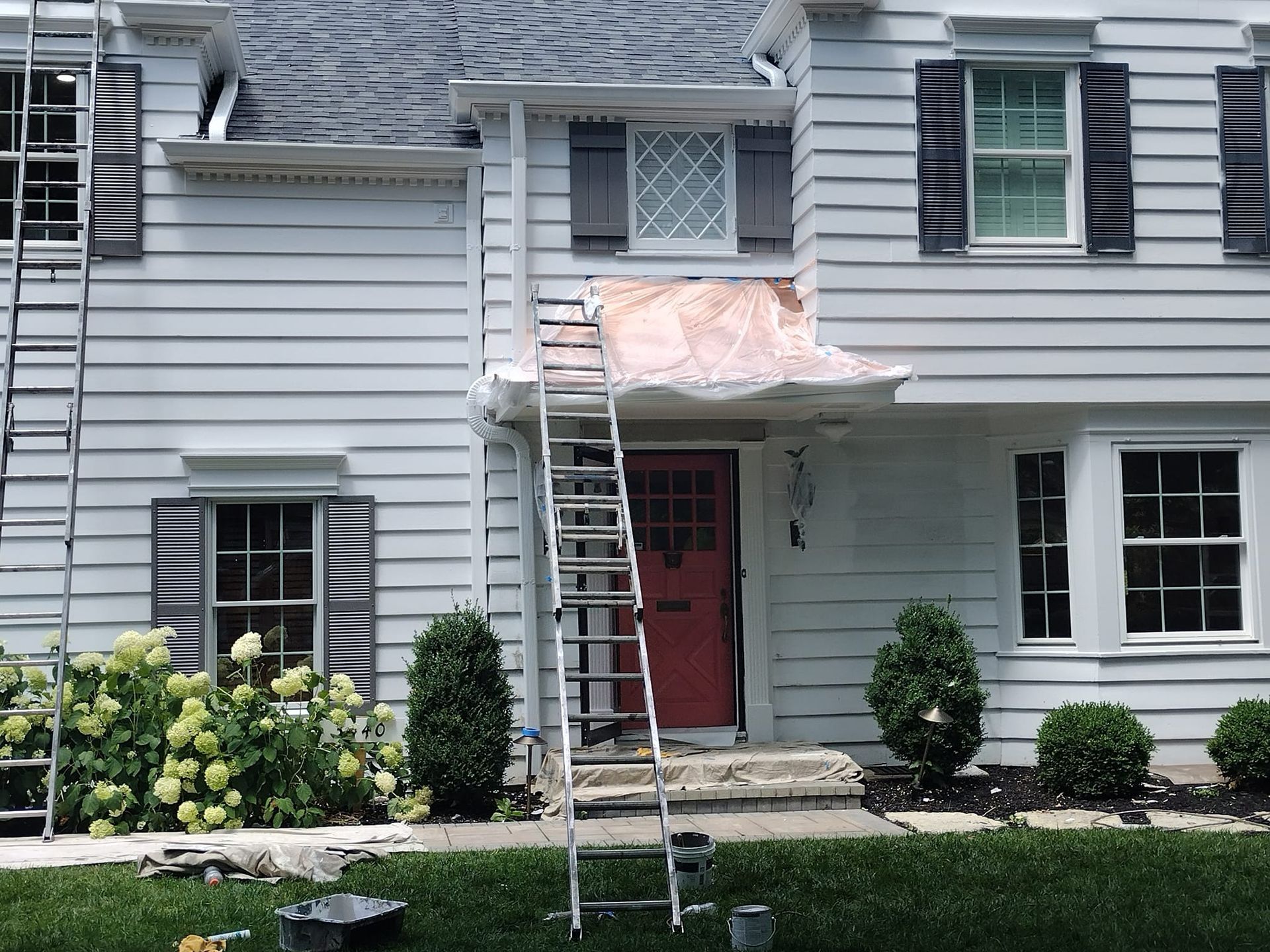 White house with ladders, red door, gray shutters. Construction in progress.