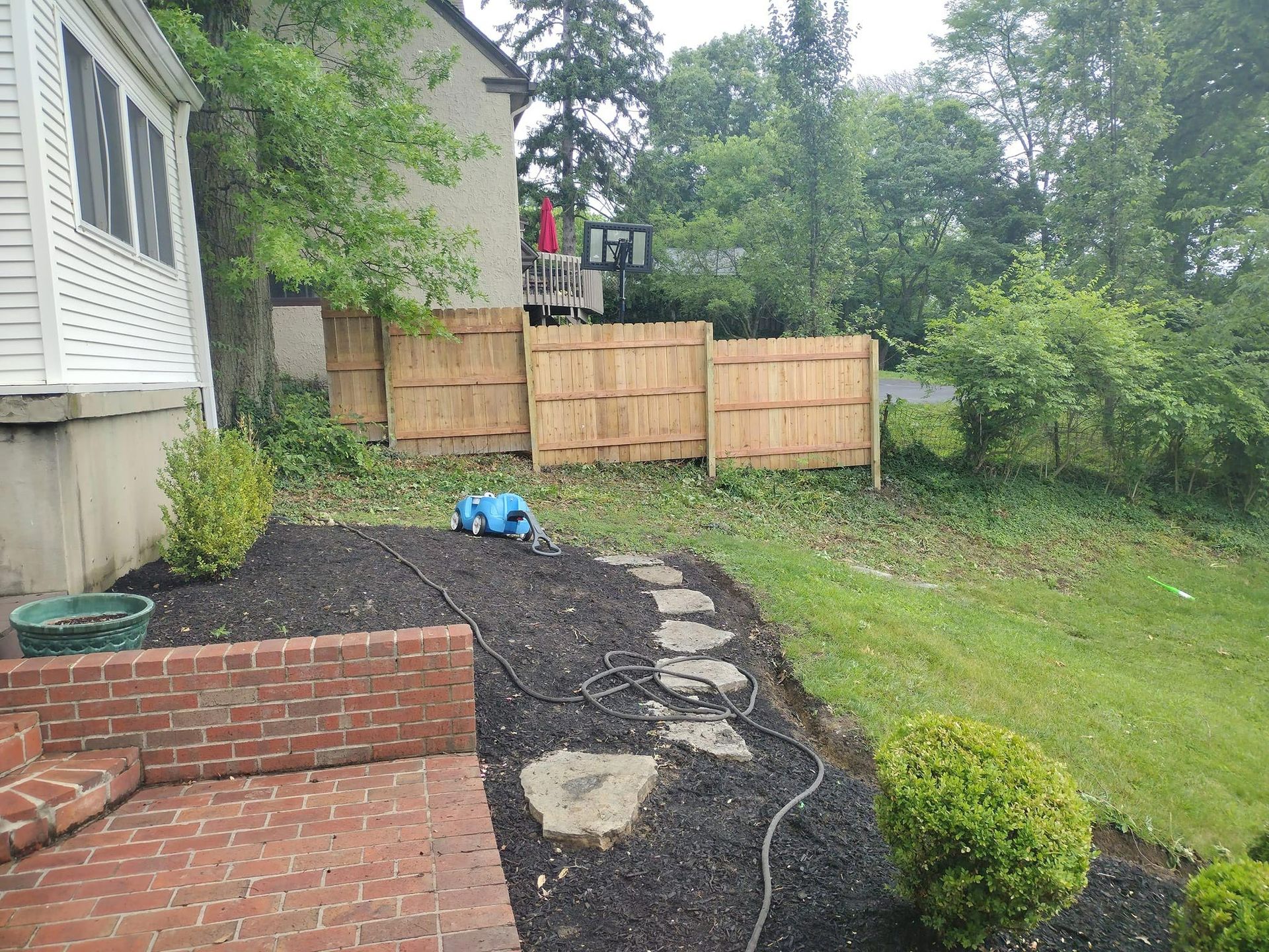 Backyard scene with a brick patio, stepping stones, and a new wooden fence.