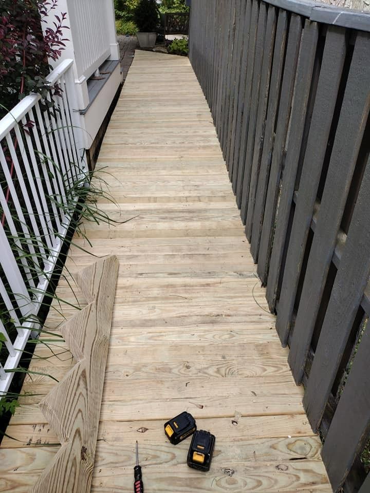 Wooden ramp with tools, next to white railing and gray fence.