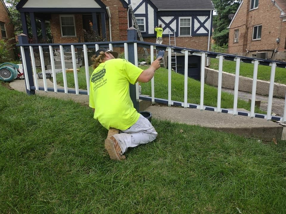 Person painting a white and blue fence in front of a house.