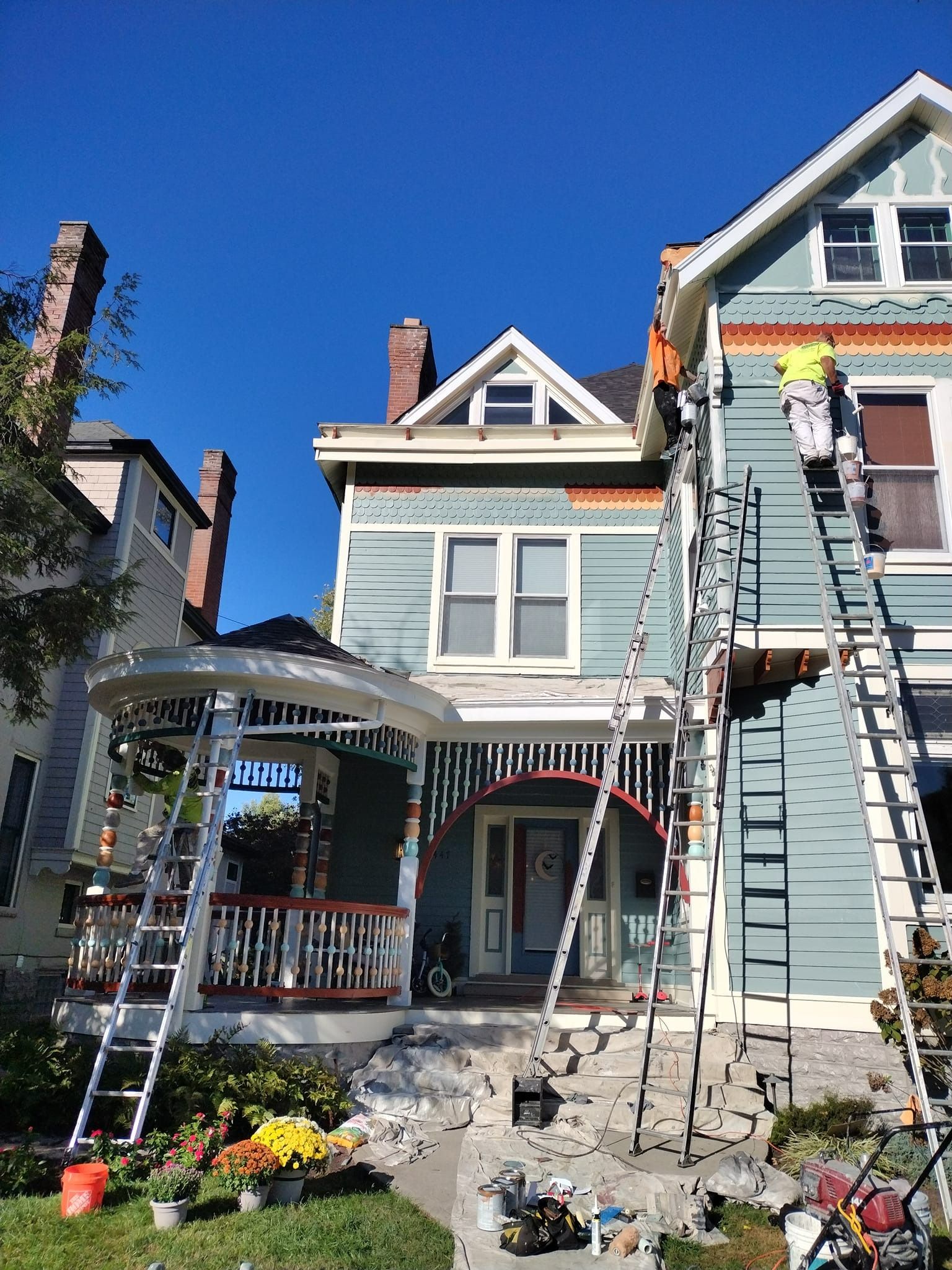 House being painted, workers on ladders. Blue and white siding, red trim. Sunny day.