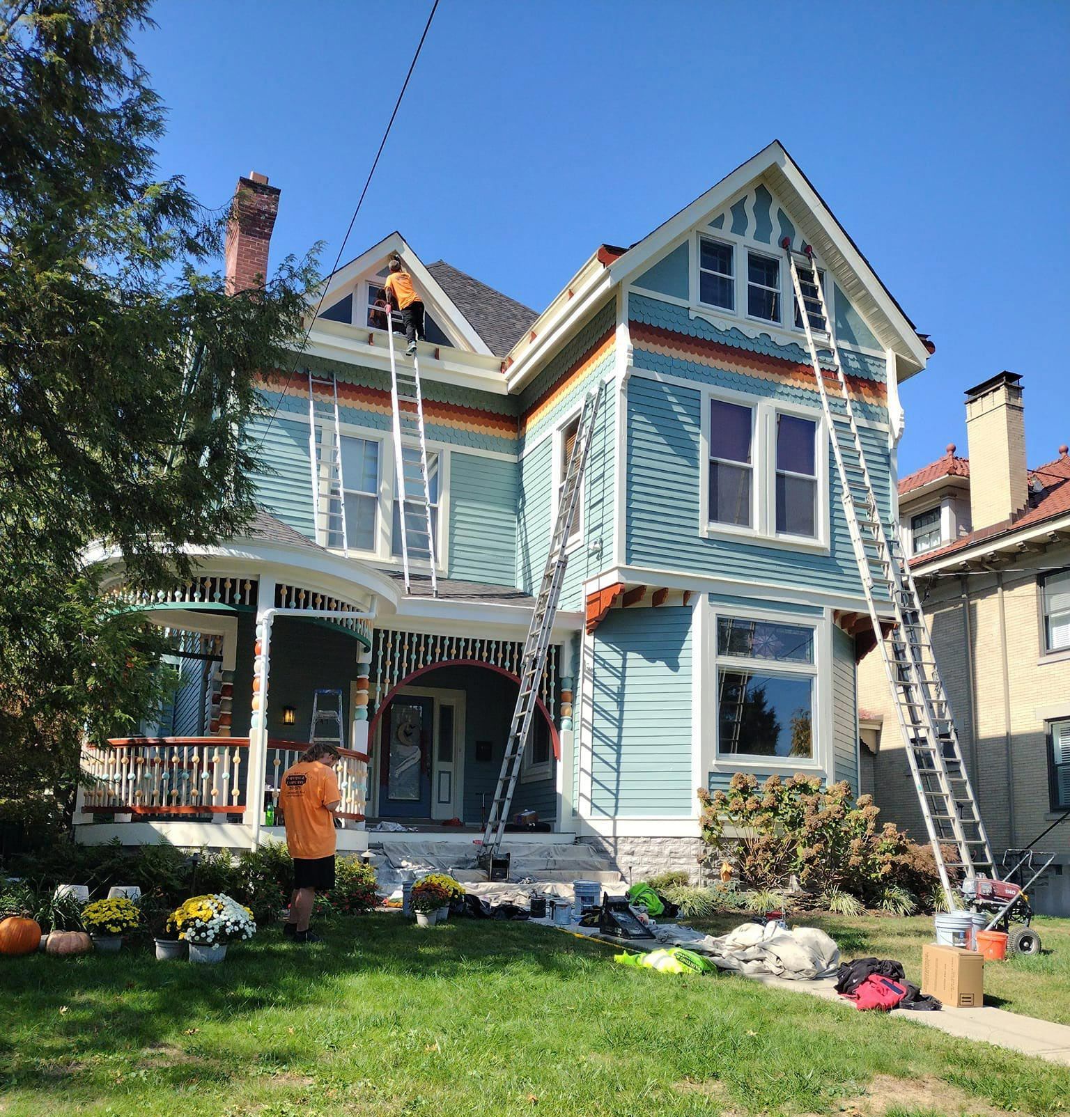 House being painted blue and orange with ladders and workers outside.