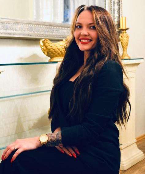 Eine Frau in einem schwarzen Kleid sitzt vor einem Kamin.