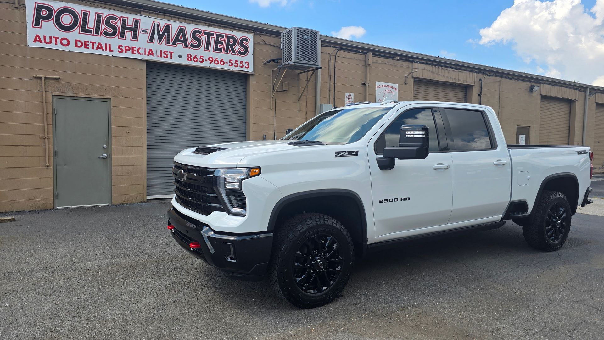 White Chevy pickup truck parked in front of a brick building labeled