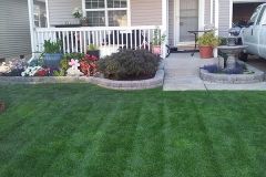 Lush green lawn, flowerbeds, and a home's front porch with a fountain, plants, and a parked truck.