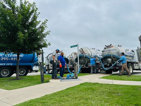 Septic tank trucks and workers on a residential street, pumping waste from an underground system.