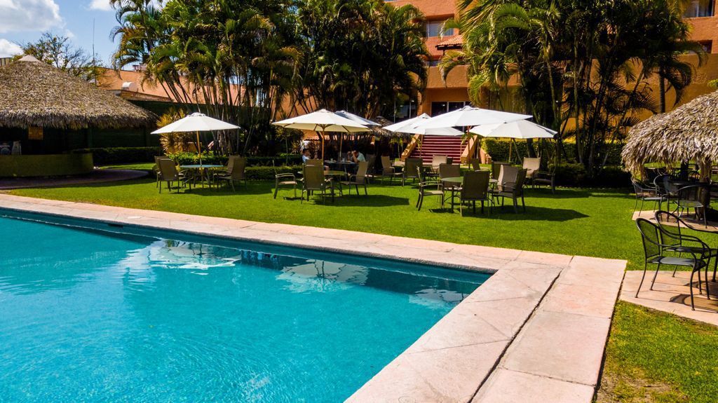 Una gran piscina rodeada de mesas, sillas y sombrillas en HOTEL DE CUAUTLA,  Cuautla, Morelos