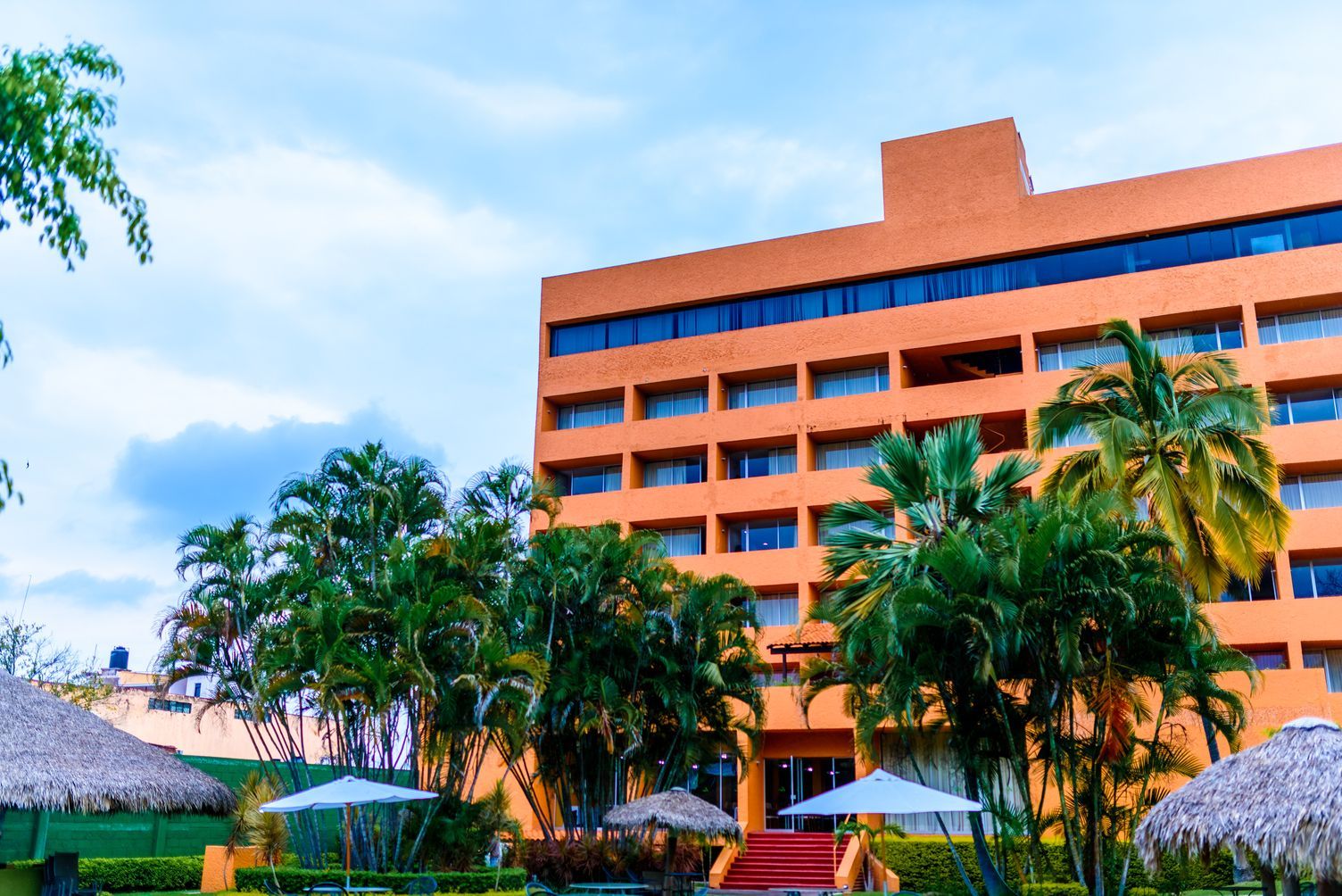 Edificio HOTEL DE CUAUTLA rodeado de palmeras y sombrillas.