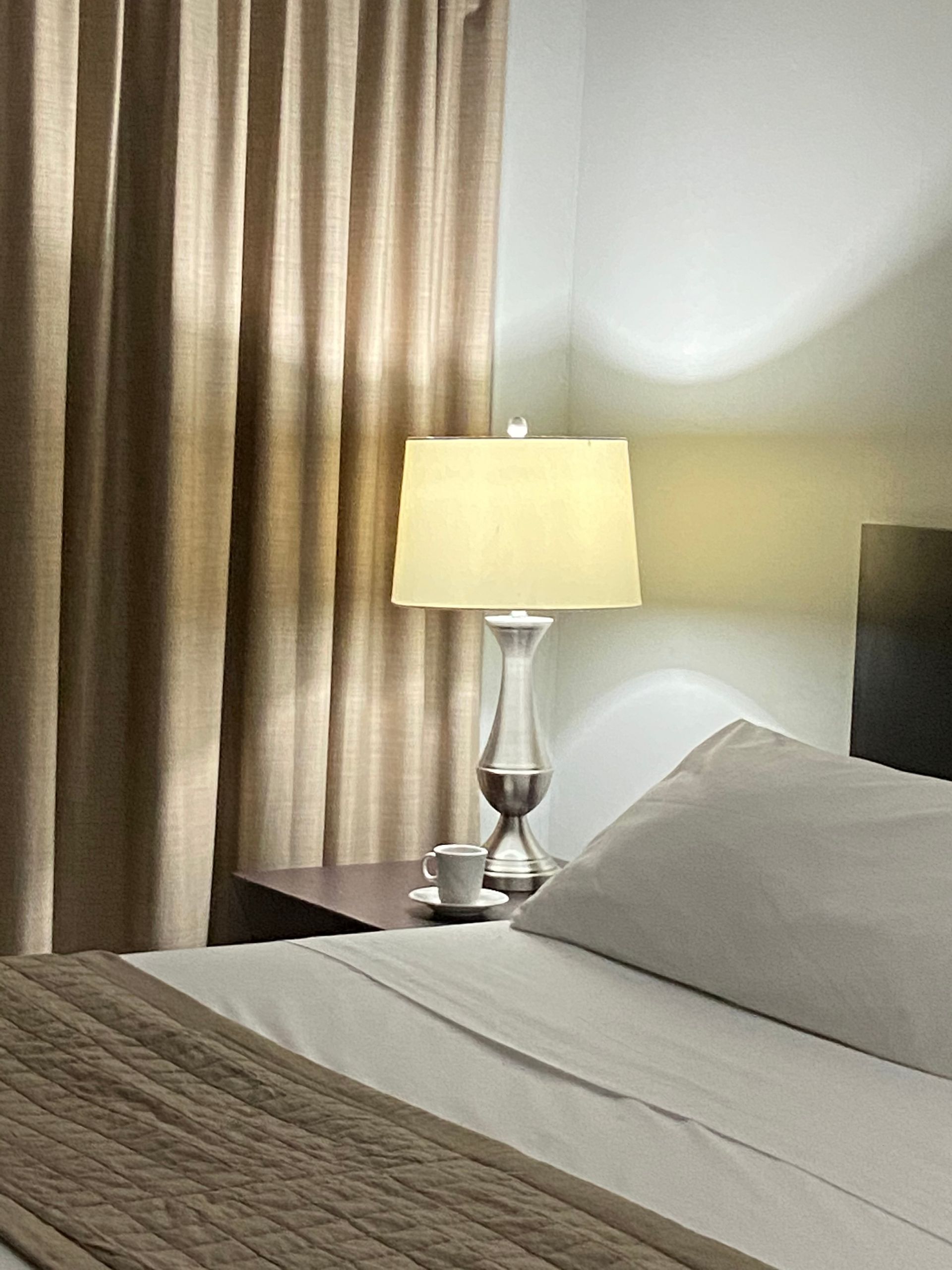 Un dormitorio con cama, mesita de noche, lámpara y cortinas.