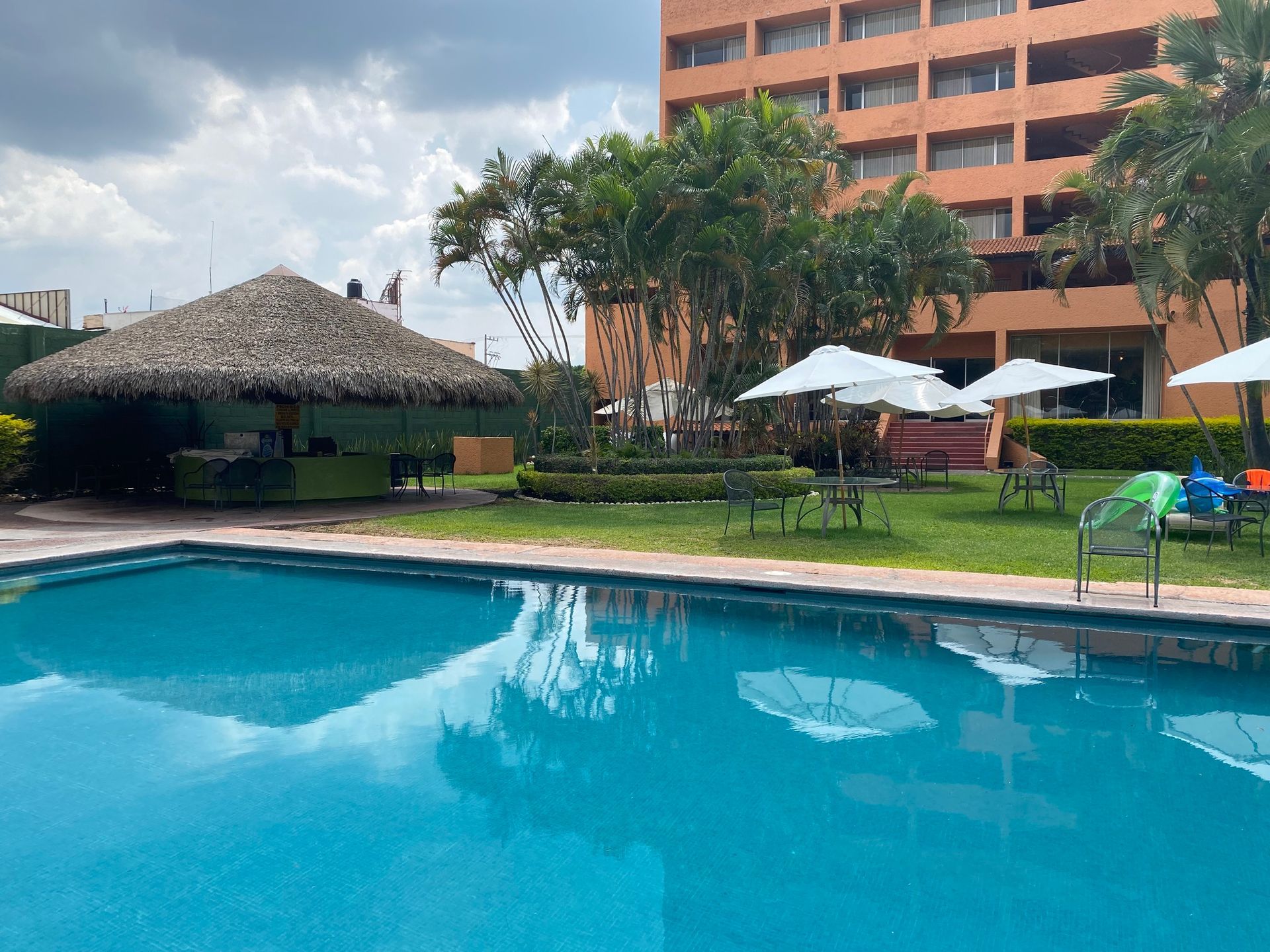 Una gran piscina con sombrillas y una cabaña de paja al fondo en HOTEL DE CUAUTLA,  Cuautla, Morelos