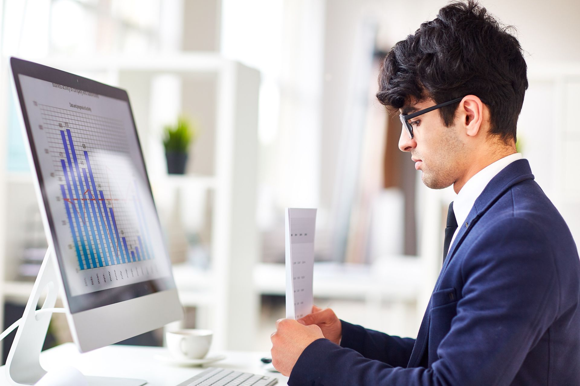 A man in a suit is sitting at a desk in front of a computer.