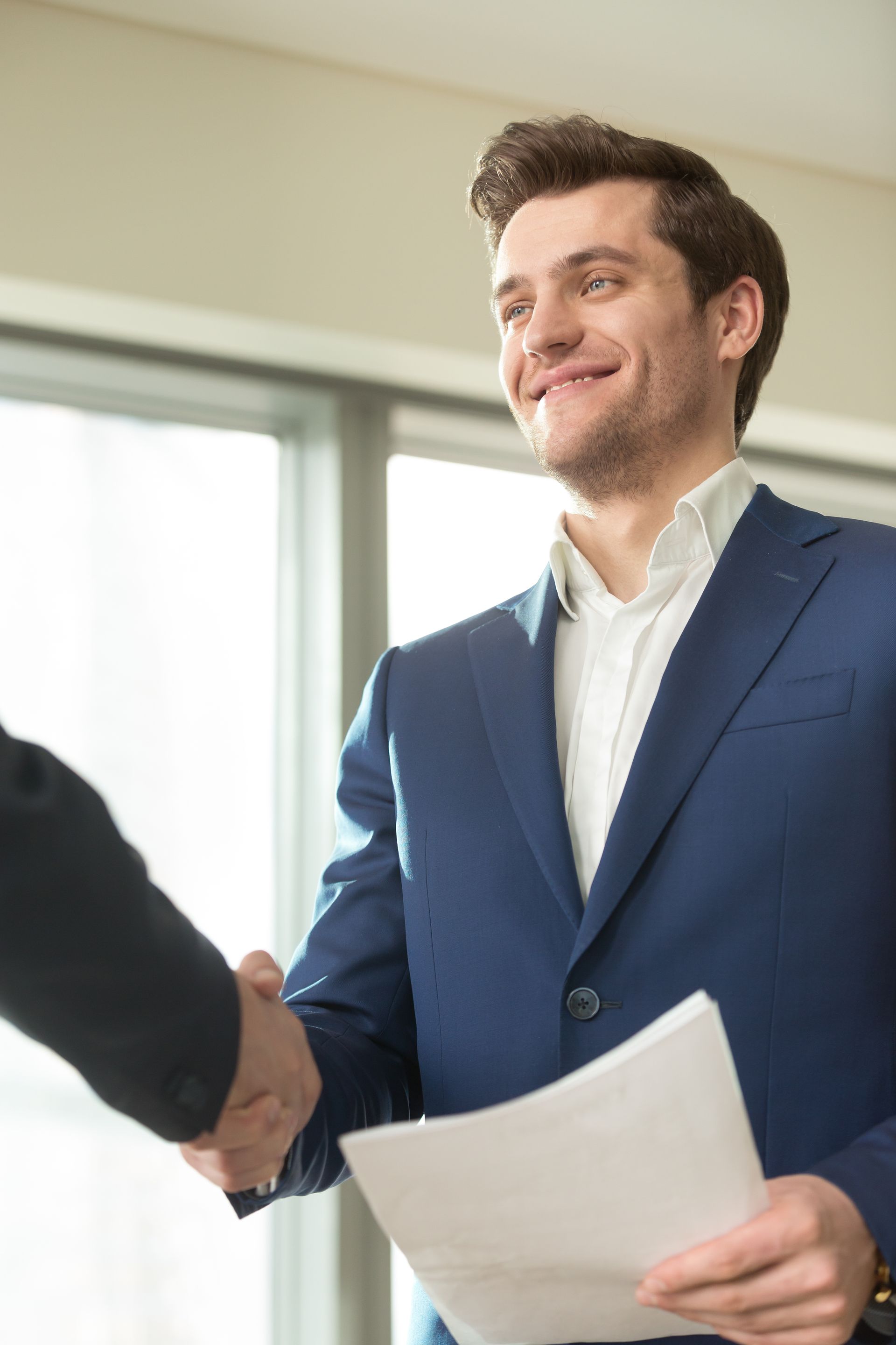 A man in a suit is shaking hands with another man while holding a piece of paper.