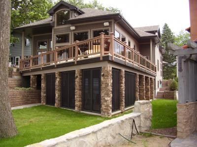 Two-story house with stone columns, deck, and large windows overlooking a green lawn.