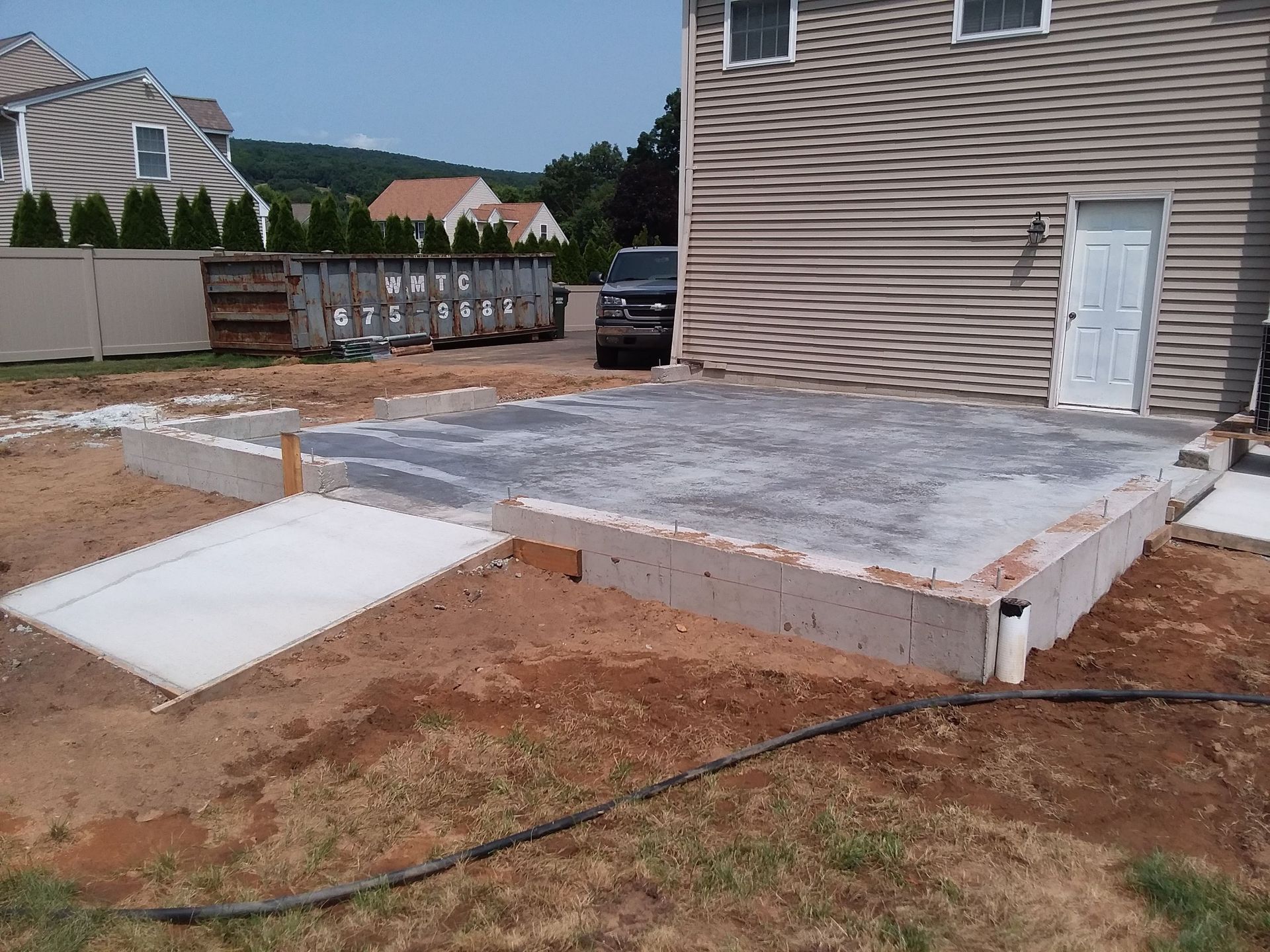 Concrete foundation construction in backyard with access ramp and house in background.