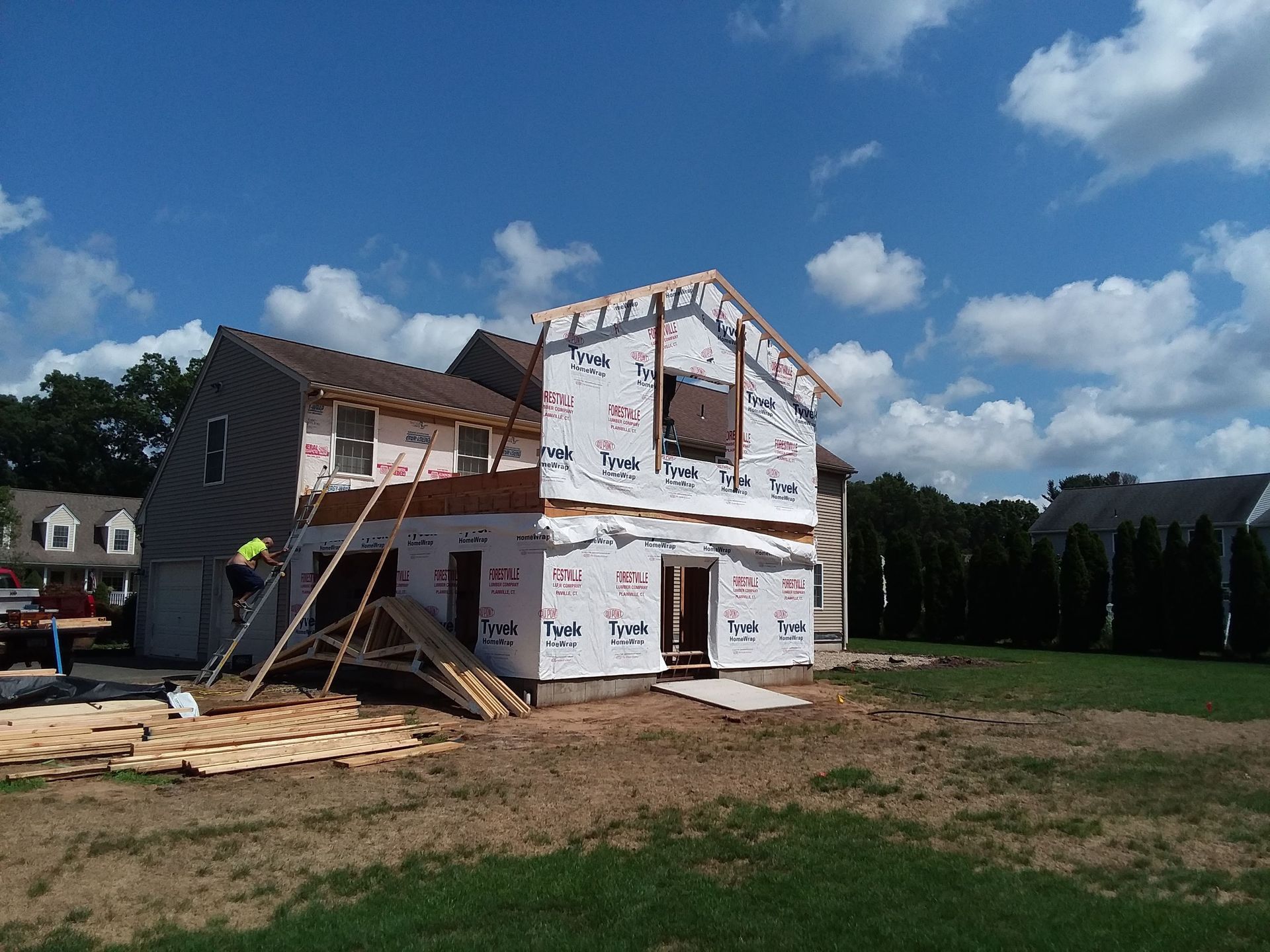 House under construction; workers on scaffolding, exterior wrapped in Tyvek, against a blue sky.
