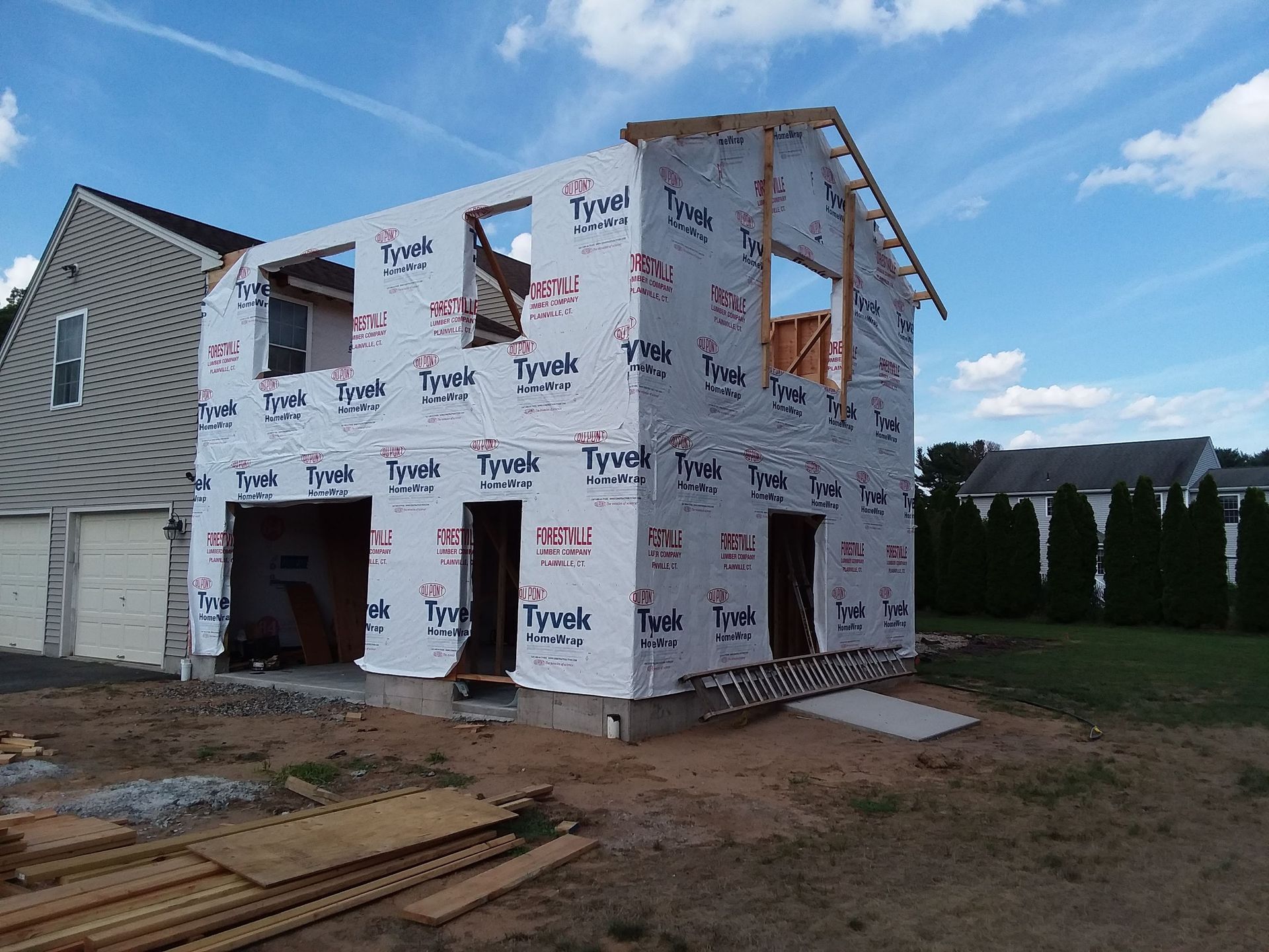 Two-story building under construction; Tyvek wrap, wood framing, unfinished roof, garage doors.