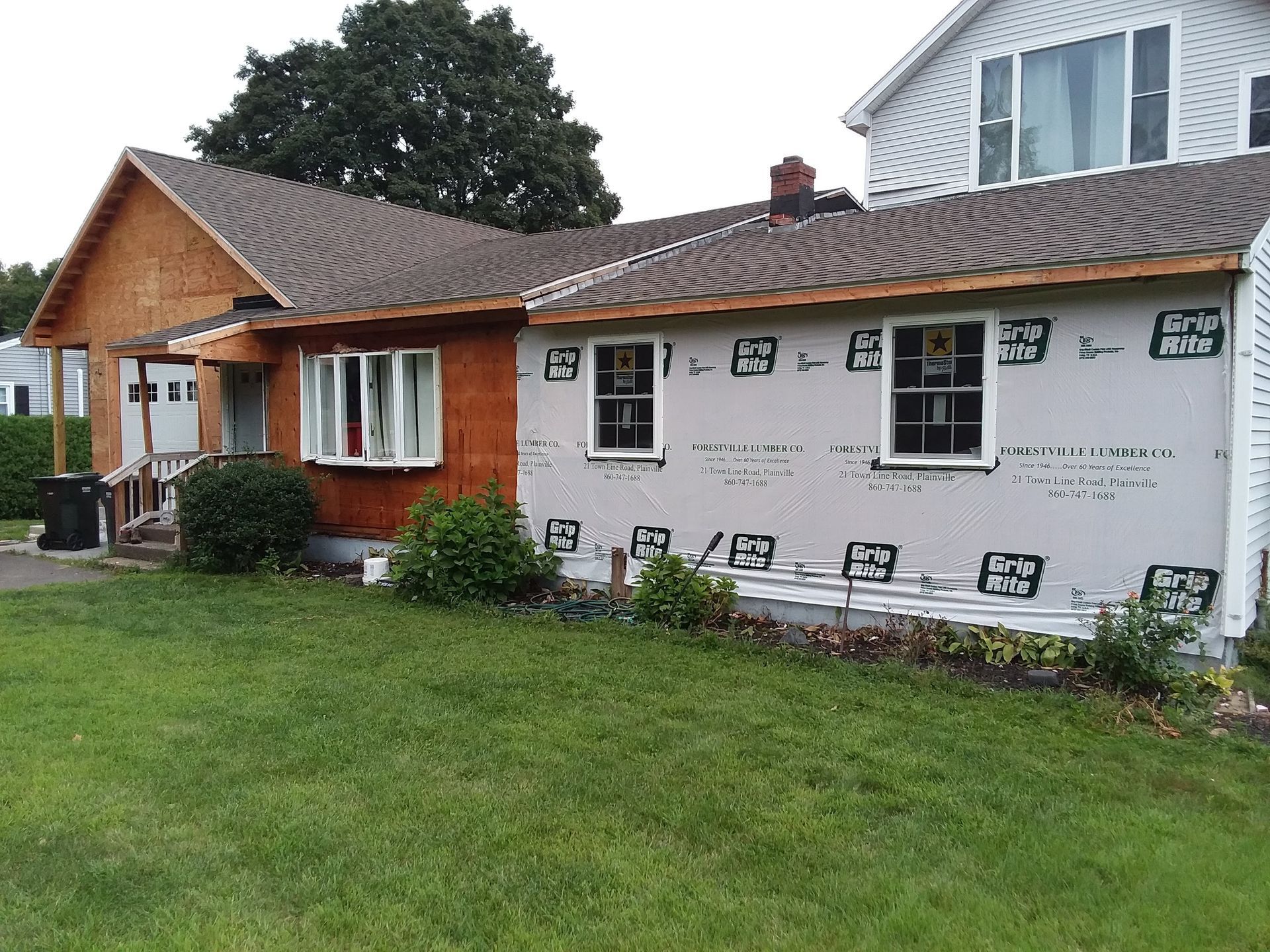 House under renovation; new siding and framing visible, brown and grey tones, green lawn.