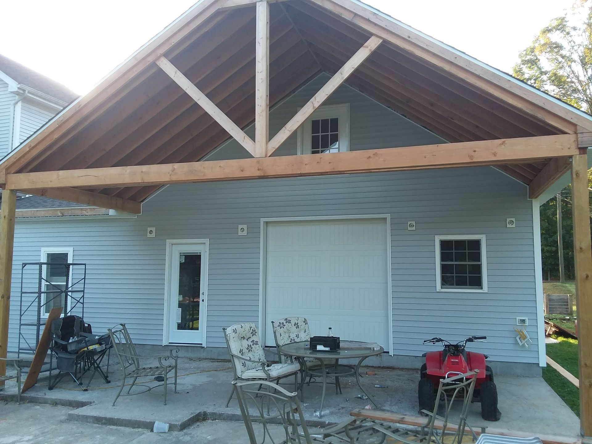 Attached porch roof over a garage with light blue siding. Includes a table and chairs on the patio, plus an ATV.