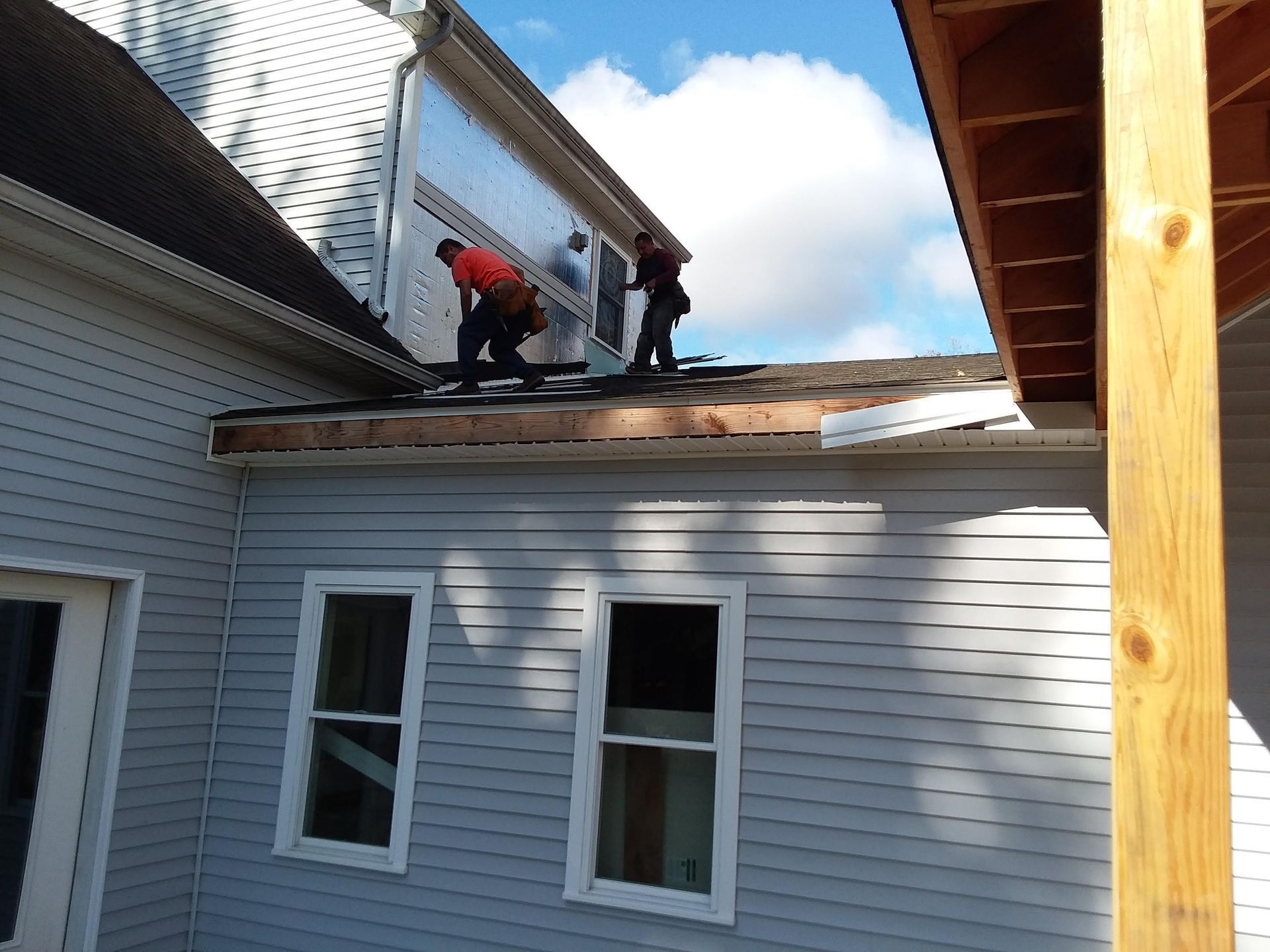 Three workers on a roof, preparing for a roofing project on a two-story house.