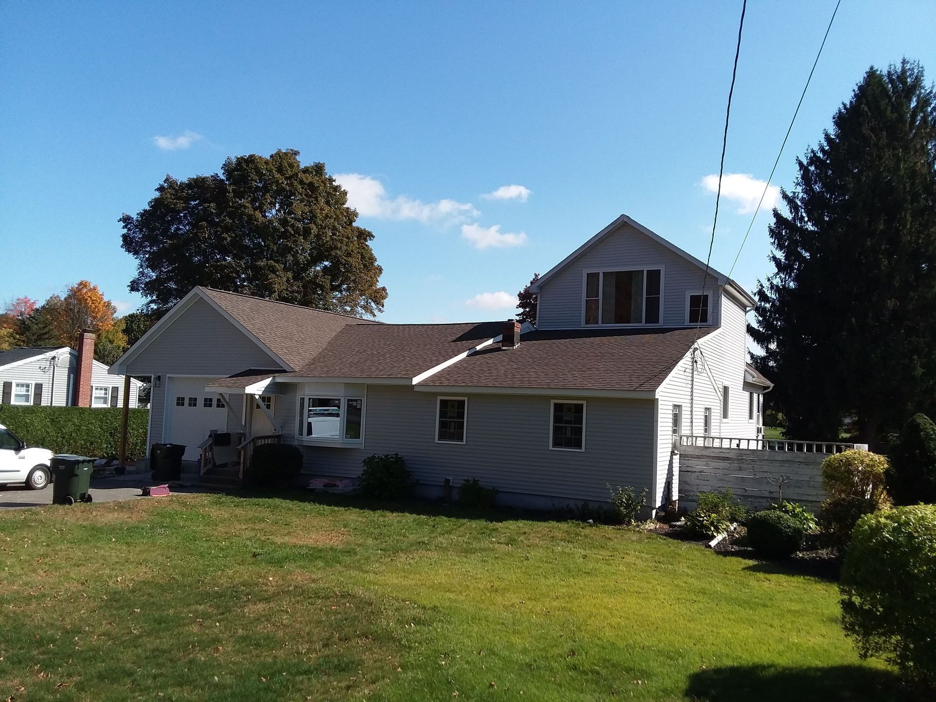 House with grey siding, brown roof, and green lawn under a blue sky.