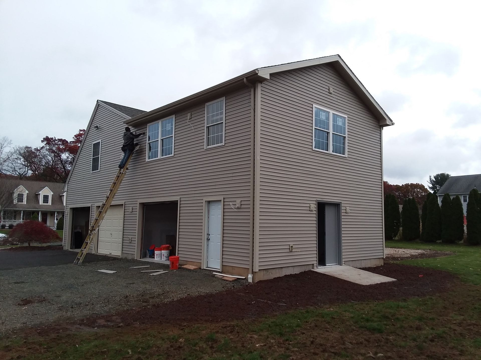 Two-story building under construction; beige siding, garage doors open. A person on a ladder is visible.