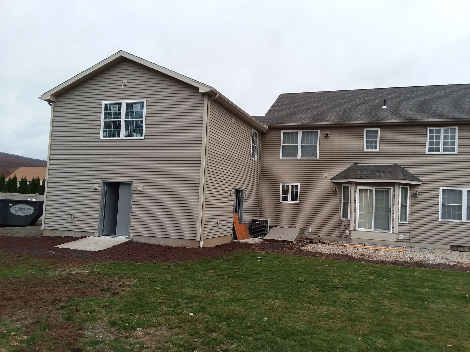 Back view of a house with a newly built addition, tan siding, and green lawn.