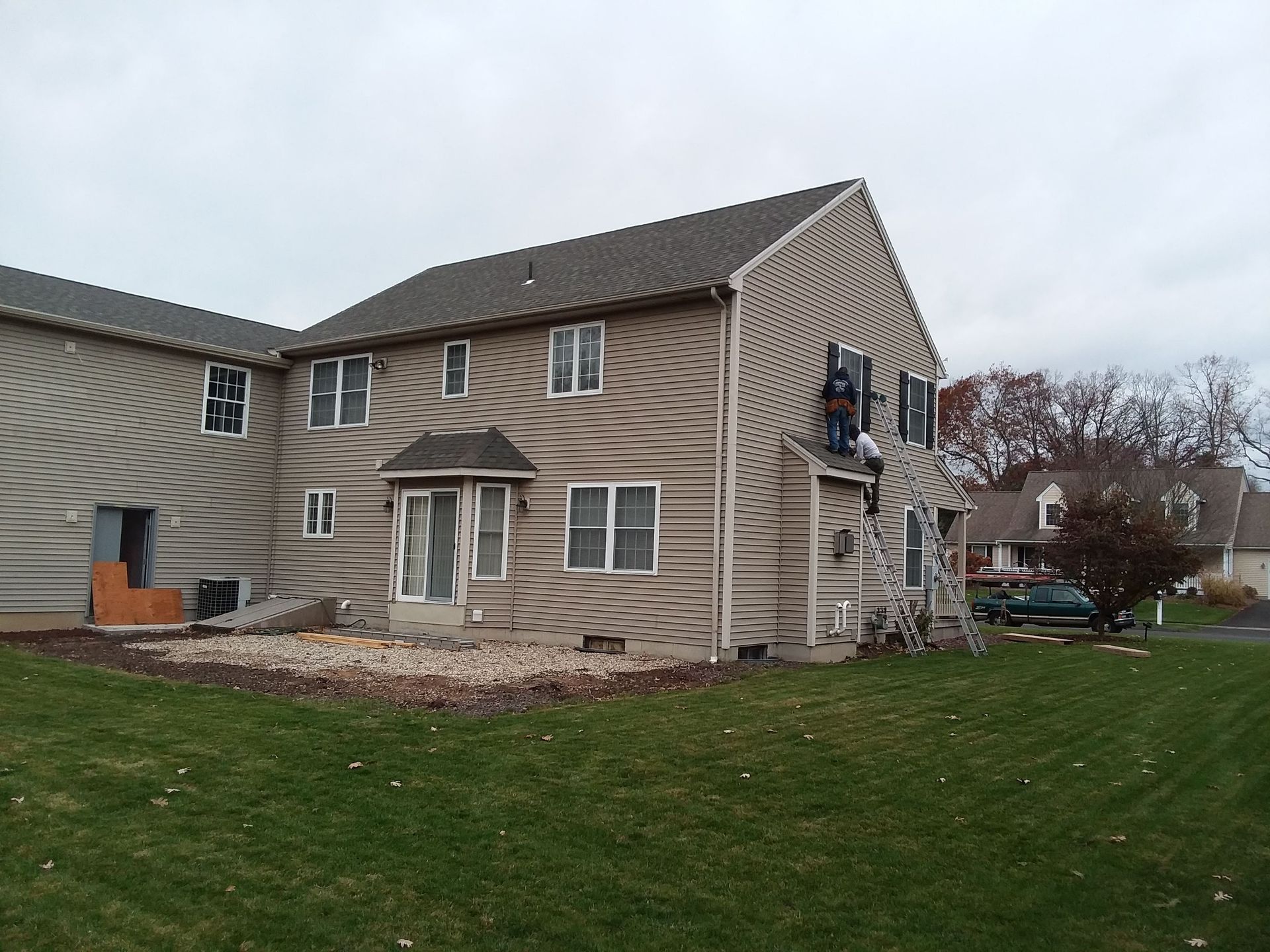 Brown multi-unit building with tan siding, lawn, and cloudy sky.
