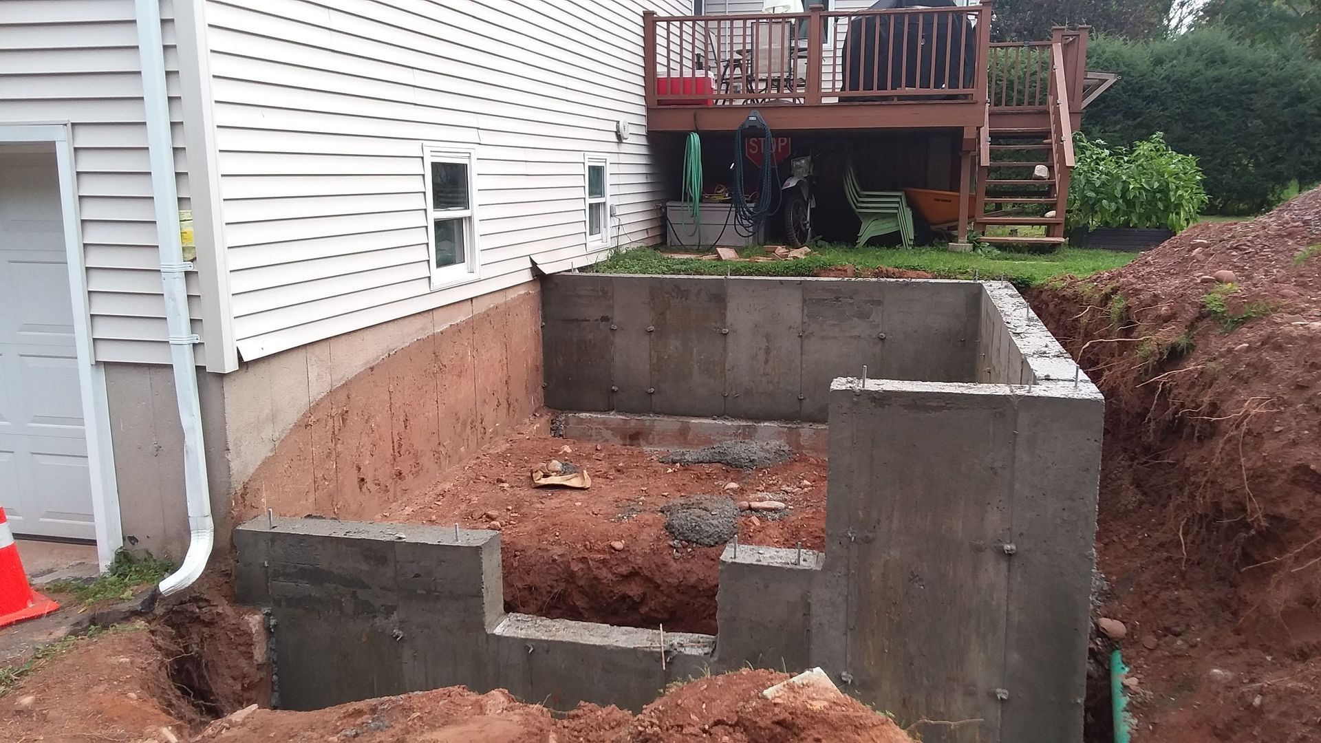 Concrete foundation construction near a house with a wooden deck and excavation.