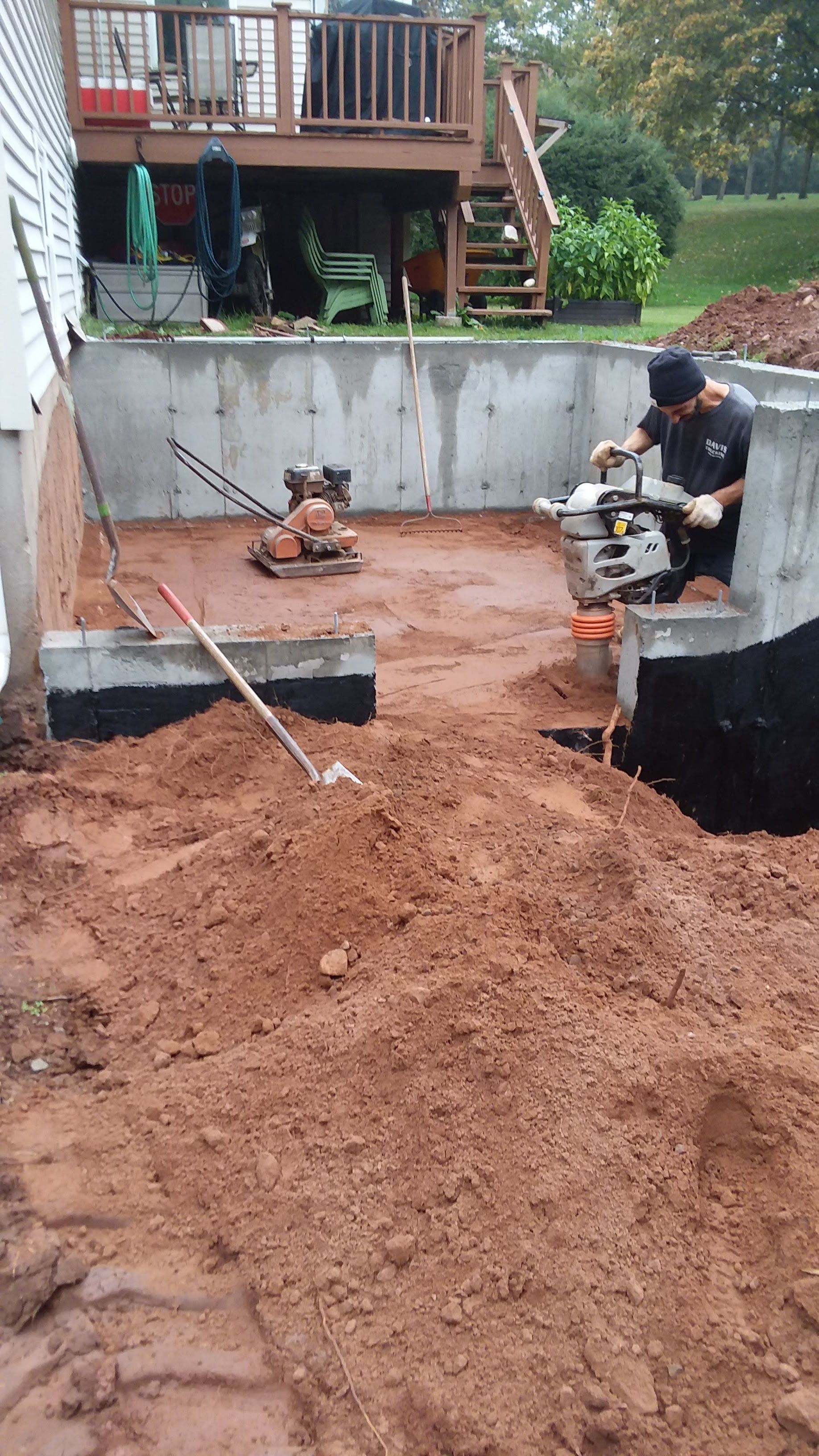 Man operating a saw, cutting material in an outdoor construction project. Brown dirt, concrete walls, deck in background.